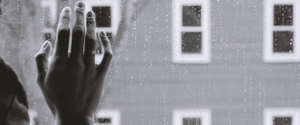 Person holding hand on window in rain
